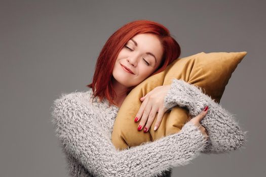 Studio portrait of a woman in a sweater hugging a pillow. The concept of fatigue or odicancy. Isolated on a gray background.