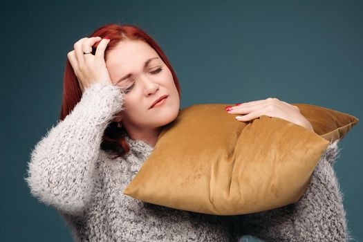 Ill and tired woman having terrible headache. Beautiful model holding one hand on forehead and with another hand holding brown pillow on shoulder. Concept of illness and advertisement.