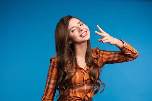 Front view of happy young model wearing orange checkered shirt showing piece, looking at camera, and posing on bue isolated background in studio. Concept of lifestyle and happiness.