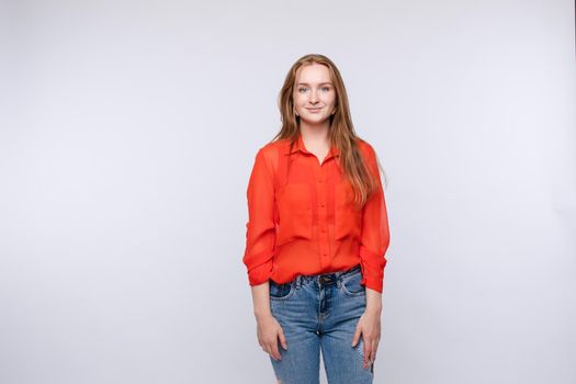 Cropped view of young woman wearing red shirt and jeans standing at grey isolated background in studio. Longhaired girl looking at camera, smiling and posing in studio. Concept of lifestyle.