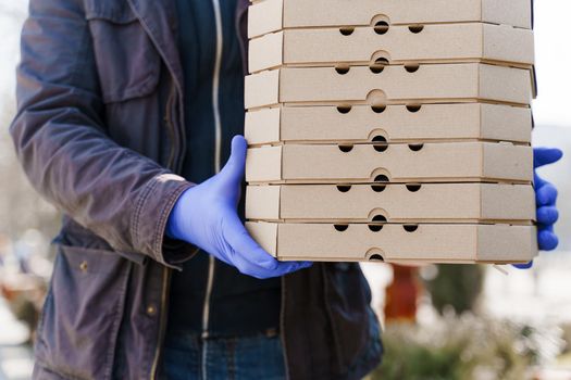 Food delivery courier in medical gloves with many boxes of pizza. Stay at home because coronavirus covid 19 killing people. Take away food.