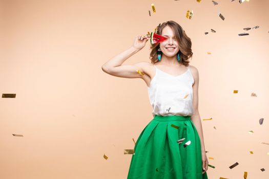 Playful elegant smiling woman posing with piece watermelon candy surrounded shining colorful confetti. Happy young female having positive emotion looking at camera isolated at light studio background