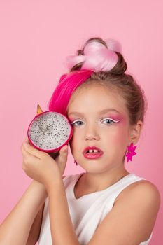 sweet Girl is holding a Pitahaya near her face. A pitaya fruit hold in hand on pink background. Tropical Dragon Fruit cut in half. space for text