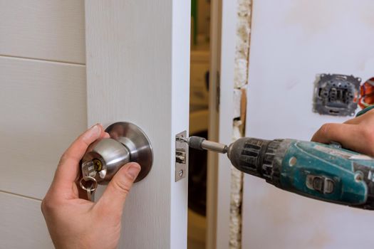Builder in installing a door lock the door of a new house hand close-up.