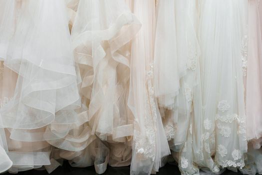 Cloth of wedding dresses made of silk chiffon, tulle and lace. Beautiful White cream bridal dress on hangers in wedding salon. Pearls and crystals pendants on the sleeves of a wedding dress