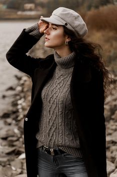 Beautiful girl in a black coat and a gray woolen cap near the lake. Traveling in your country.