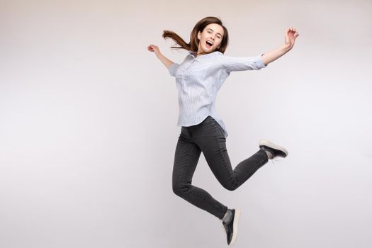 Full length isolate portrait of positive brunette young girl in jeans and t-shirt and sneakers jumping over yellow background. She is smiling at camera.