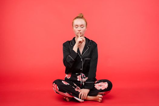 Young girl in black pijama sitting on floor and meditating with closed eyes. Beautiful happy woman in casual clothes doing yoga and practicing breathing. Pretty relaxed lady caring about her health.