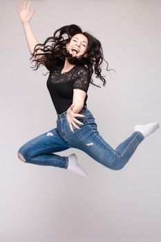 Full length isolate portrait of positive brunette young girl in jeans and t-shirt and sneakers jumping over yellow background. She is smiling at camera.