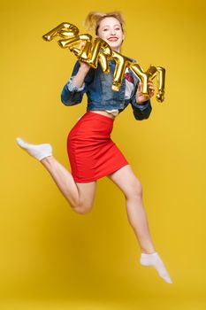 Full length isolate portrait of positive brunette young girl in jeans and t-shirt and sneakers jumping over yellow background. She is smiling at camera.