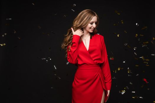 Front view of elegant woman wearing long black dress looking at camera and smiling on black isolated background. Attractive blonde with long legs posing in studio. Concept of party and beauty.