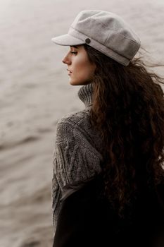 A beautiful girl close-up in a black coat and a gray woolen cap near the lake. Traveling in your country