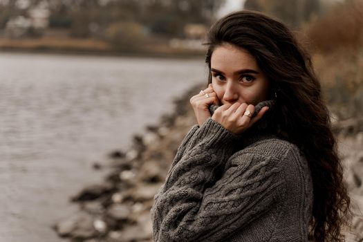 Girl with curly hair on the background of birch with stones and lake in autumn.