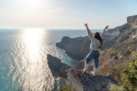 Woman tourist enjoying the sunset over the sea mountain landscape. Sits outdoors on a rock above the sea. She is wearing jeans and a blue hoodie. Healthy lifestyle, harmony and meditation.