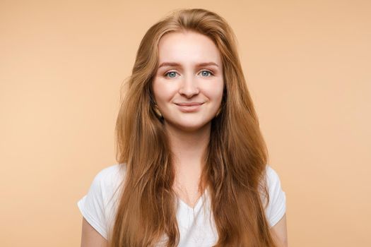 Portrait of beautiful smiling young red hair girl posing looking at camera medium close-up. Attractive European friendly woman having positive emotion isolated at yellow studio background