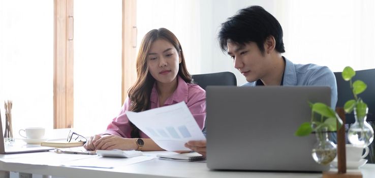 Two Cheerful Asian young business people working together using a tablet at a modern office.doing planning analyzing the financial report, business plan investment, finance analysis concept.