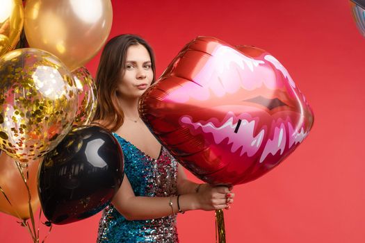 Full length studio portrait in sexy sparkling cocktail dress with red lips. She is posing with lips air balloon. Isolate on red background.