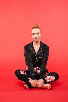 Young girl in black pijama sitting on floor and meditating with closed eyes. Beautiful happy woman in casual clothes doing yoga and practicing breathing. Pretty relaxed lady caring about her health.