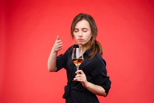 Cropped view of female standing on re isolated background and keeping glass of wine. Young beautiful woman with closed eyes smelling champagne. Concept of alcohol and scent.