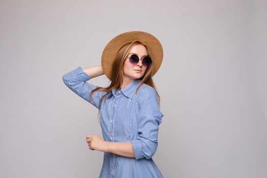 Front view of bright young girl wearing straw hat and glasses posing on isolated background in studio. Female tourist, looking at camera and smiling. Concept of summer.