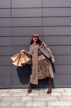 A happy shopaholic girl keeps her bags near the shopping center. A woman near the store is happy with her purchases, holding bags. Dressed in a leopard print dress. Consumer concept