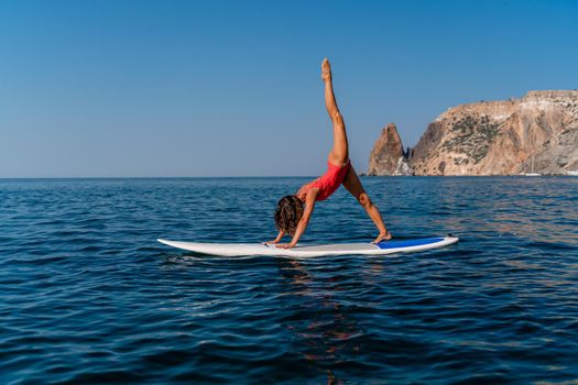 Sporty girl on a surfboard in the sea on a sunny summer day. In a red swimsuit, she sits in the splits on the sap. Summer entertainment on Stortom by the sea.