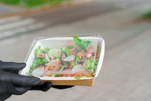 Green salad with veal and vagatables. Safety delivery with mask and black medical gloves at quarantine. Salad in eco thermo box.