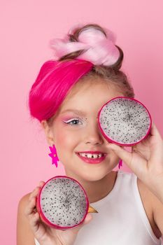Close-up portrait of pretty girl with pink hairstyle with dragon fruit on pink background. Studio shot of charming tween girl with pink make up enjoying juicy red pitaya. exotic Pitahaya fruit.
