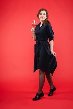 Young pretty lady in casual clothes holding delicious drink in hands. Brunette happy girl enjoying her sweet beverage and smiling. Beautiful woman in black dress standing with glass of expensive wine.
