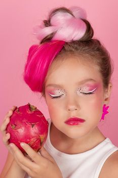 sweet Girl is holding a Pitahaya near her face. A pitaya fruit hold in hand on pink background. Tropical Dragon Fruit cut in half. space for text