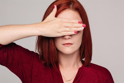 Beautiful young lady with closed eyes holding her hand near head. Clouse up of pretty red haired woman in bordo blouse with headache. Sadly girl touching her hair by hand and thinking about problem.