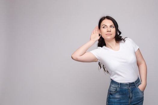 Studio portrait of curious brunette girl in multicolored top listening to the news or gossips with her ear.