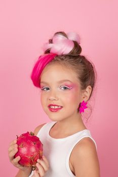 Close-up portrait of pretty girl with pink hairstyle with dragon fruit on pink background. Studio shot of charming tween girl with pink make up enjoying juicy red pitaya. exotic Pitahaya fruit.