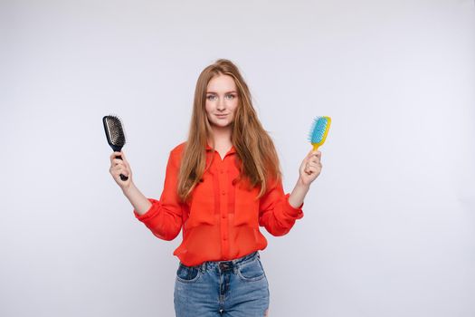 Woman holding two hairbrush posing with one half shaggy and combed hair medium shot. Female model showing healthy and unhealthy hairstyle care isolated at white studio background