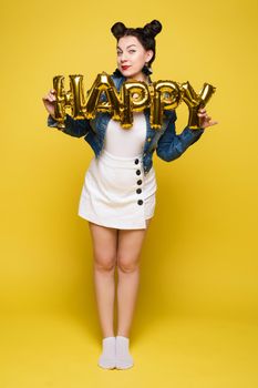 Attractive happy woman laughing holding big gold letters posing at yellow studio background medium long shot. Beautiful fashionable young girl relaxing having positive emotion