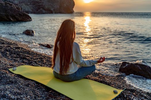 Beautiful woman with long flowing hair practices yoga on the beach, Yoga Ardha Padmasana in the half-lotus position