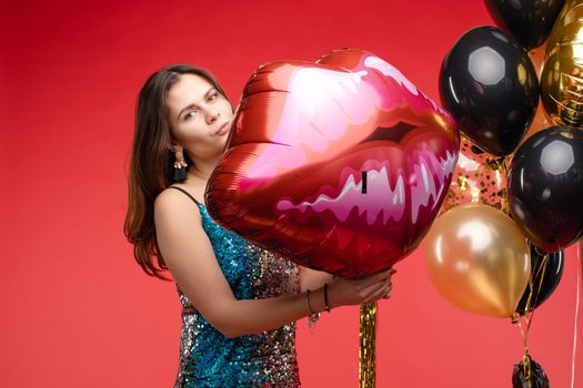 Full length studio portrait in sexy sparkling cocktail dress with red lips. She is posing with lips air balloon. Isolate on red background.