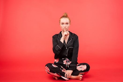 Young girl in black pijama sitting on floor and meditating with closed eyes. Beautiful happy woman in casual clothes doing yoga and practicing breathing. Pretty relaxed lady caring about her health.