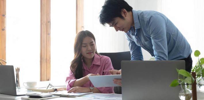 Entrepreneur Asian businessman and businesswoman discussing new business project in tablet in modern Meeting In Modern Office, Asian business casual concept..