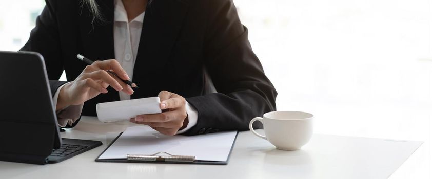 Business woman using calculator and writing make note with calculate. Woman working at office with laptop and documents on his desk.