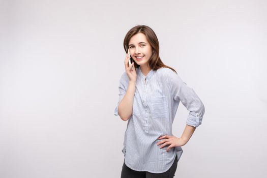 Studio portrait of pretty young brunette woman in casual shirt and jeans talking on the mobile phone and smiling at camera. Isolate on white.