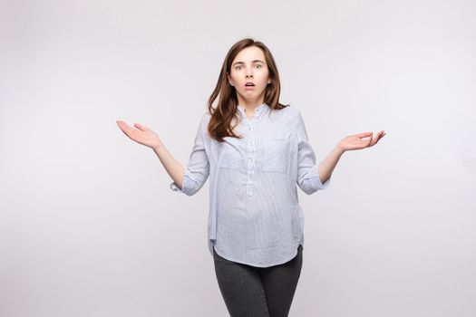 Studio portrait of brunette woman in casual clothes showing puzzlement or confusion and reacting with her arms up in amazement.