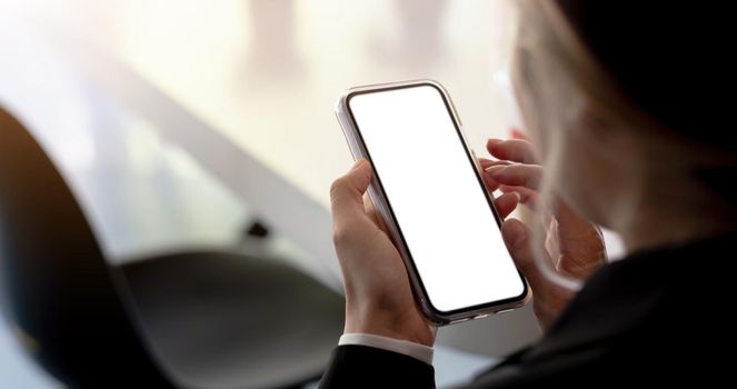 Close-up of a woman hand holding a smartphone white screen is blank the background is blurred.Mockup..