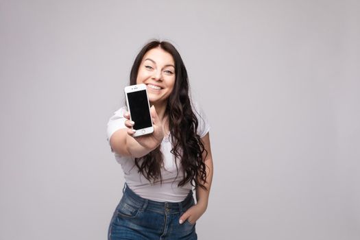 Studio portrait of beautiful caucasian brunette woman in patterned overall pointing at her smartphone with index finger. She is certain or sure about something. I know gesture.