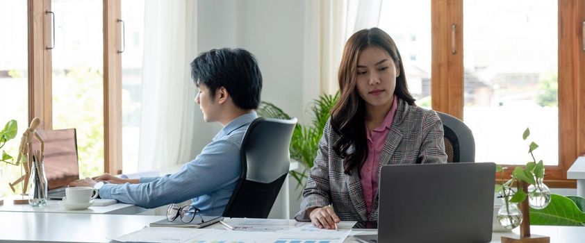 Portrait of young asian woman sitting at her desk with laptop while looking at laptop in modern office..