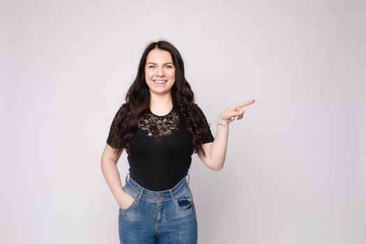 Studio portrait of beautiful caucasian brunette woman in patterned overall pointing at her smartphone with index finger. She is certain or sure about something. I know gesture.