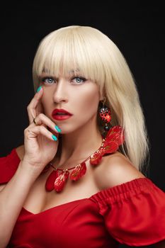 Studio headshot of stunning young adult woman with blone hair and beautiful blue eyes wearing fashionable necklace, earrings and red dress with open shoulders.