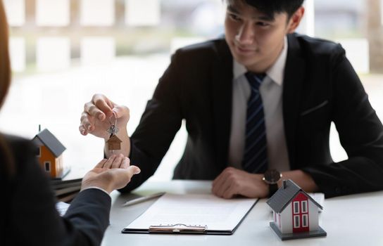 estate agent giving house keys to woman and sign agreement in office.