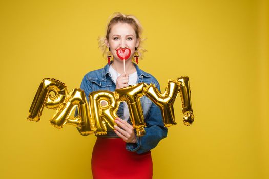 Stock photo portrait of attractive girl with red lips holding shining bright inflatable word HAPPY. Isolate on orange background.