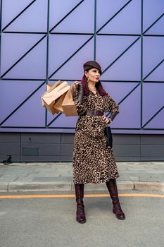 A happy shopaholic girl keeps her bags near the shopping center. A woman near the store is happy with her purchases, holding bags. Dressed in a leopard print dress. Consumer concept